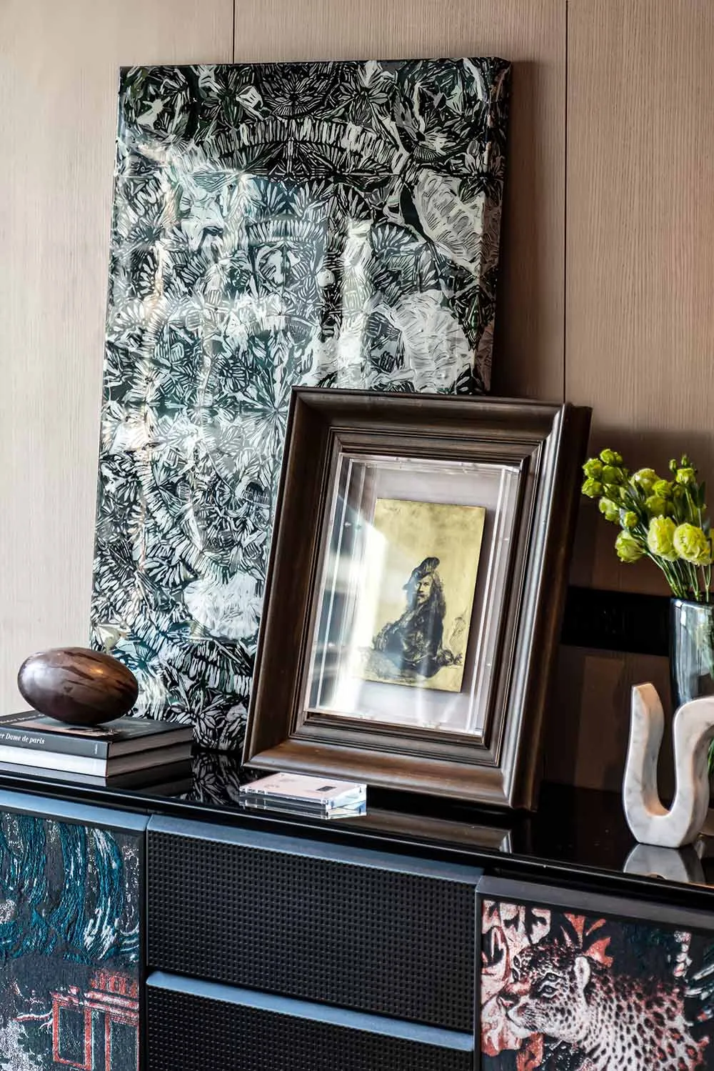 A framed antique resting on a black cabinet with decorative patterns.