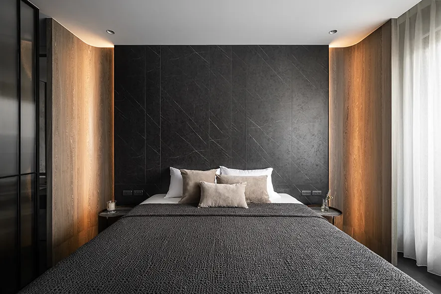 Modern minimalist bedroom with black marble walls and a neatly made bed with multiple pillows.
