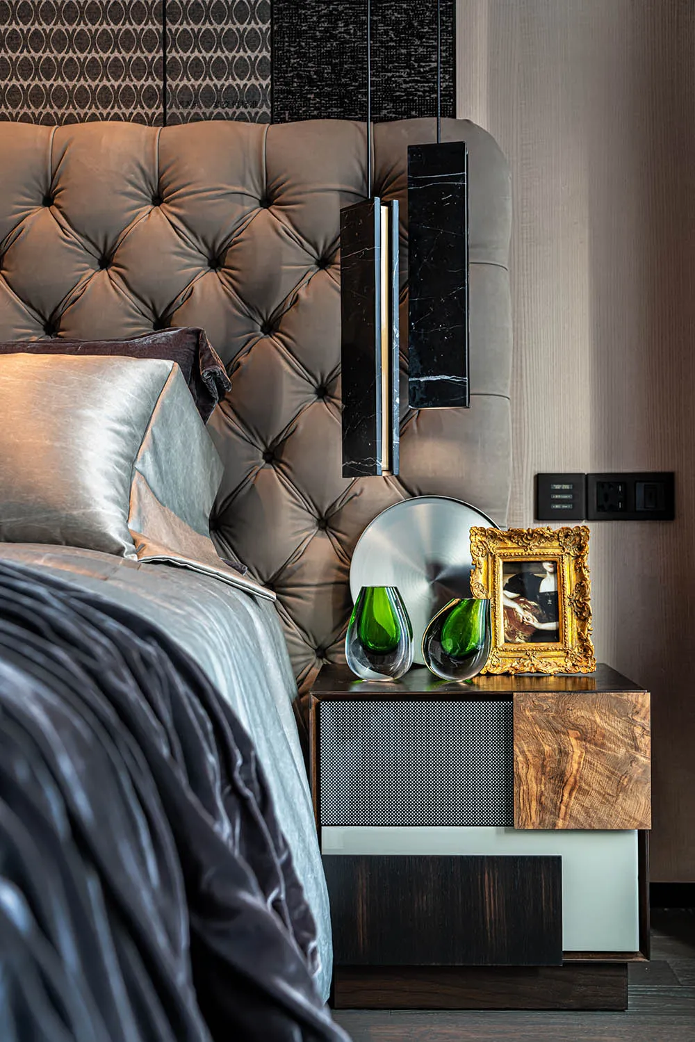 A modern bedroom featuring a tufted leather headboard, wooden nightstand, and glass vases.