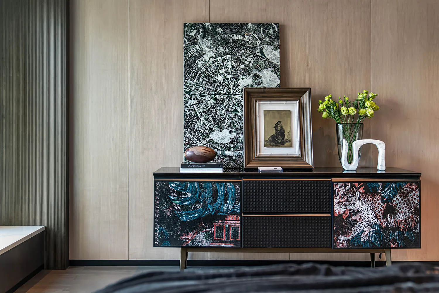 A modern living room featuring a black storage unit with colorful designs, positioned against a wooden wall with framed art.