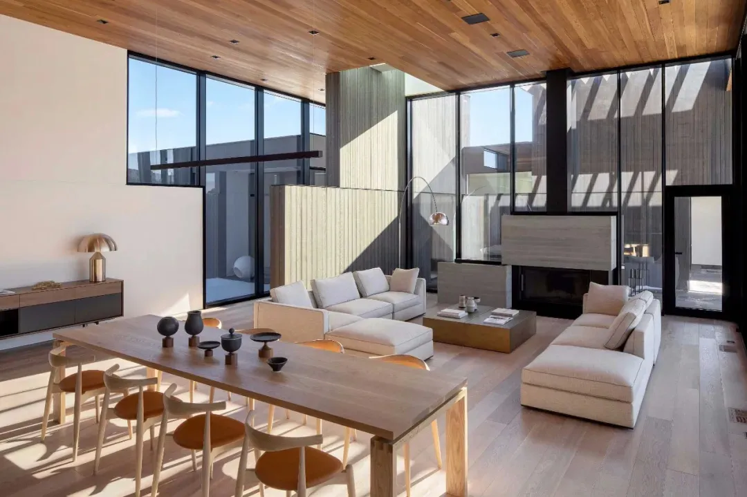 A modern living room featuring wooden furniture and flooring, with large windows allowing natural light to fill the space.