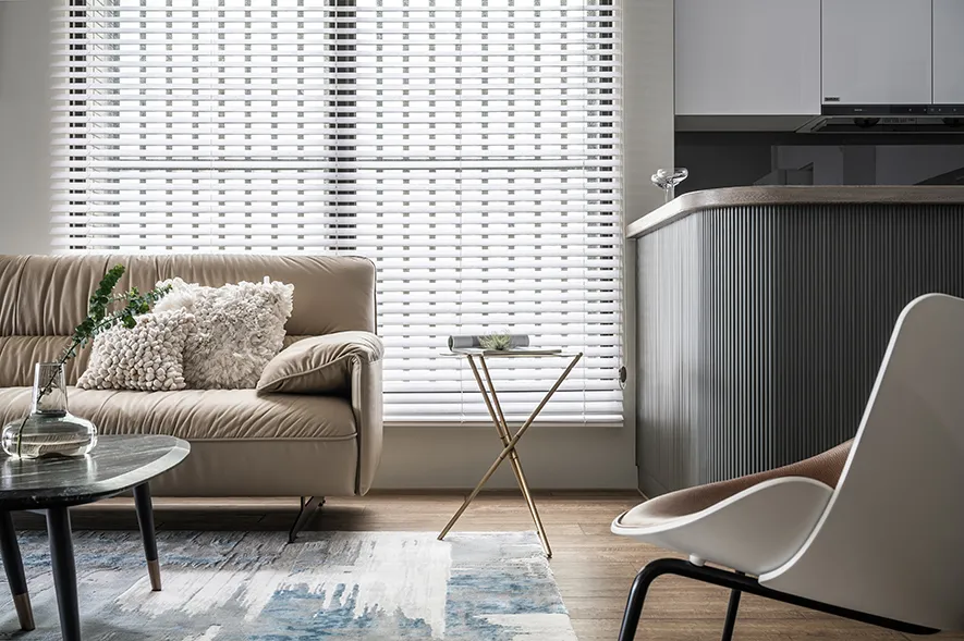 A modern living room with a beige sofa adorned with fluffy pillows, a glass coffee table, and a white armchair, featuring whi