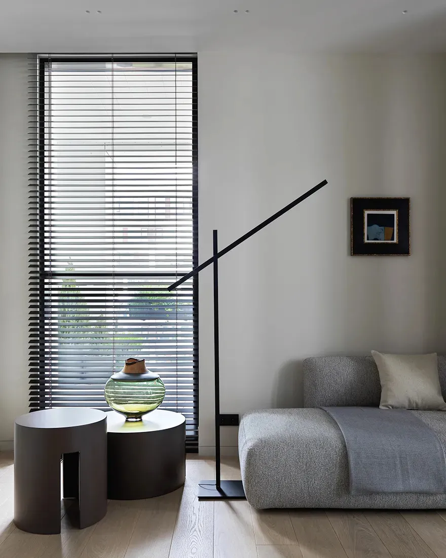 A minimalist living room featuring concrete and metal materials, with a grey couch, a black floor lamp, and a modern side tab