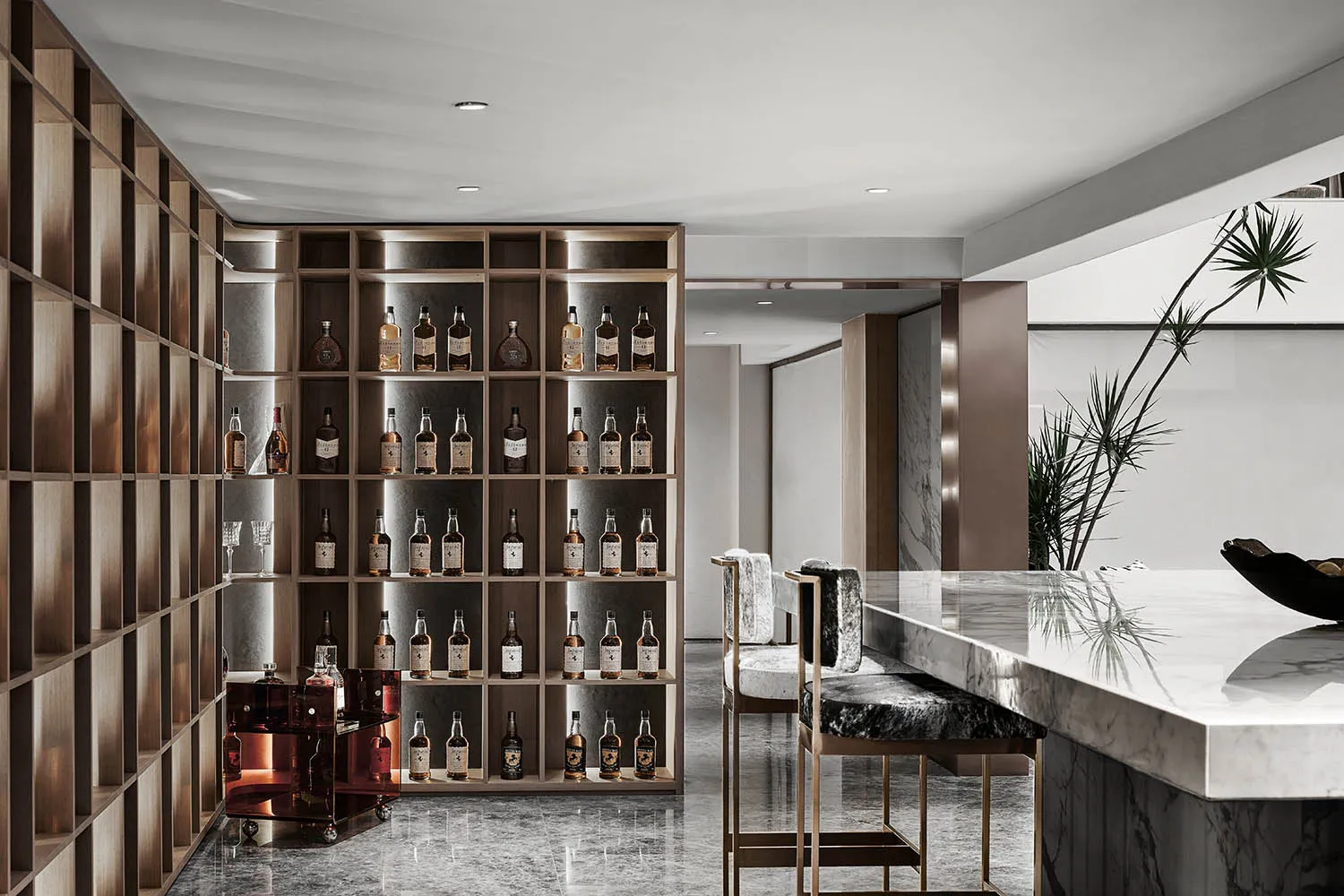 A modern bar with wooden shelves filled with bottles, a marble countertop, and concrete accents.