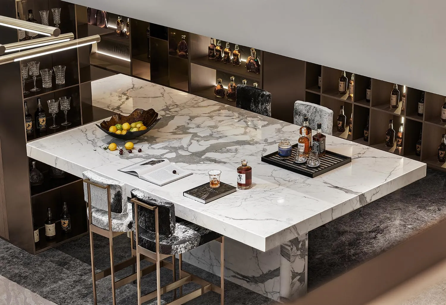 A luxurious kitchen bar featuring a marble countertop, a bowl of lemons and cherries, and a tray with bottles of alcohol.