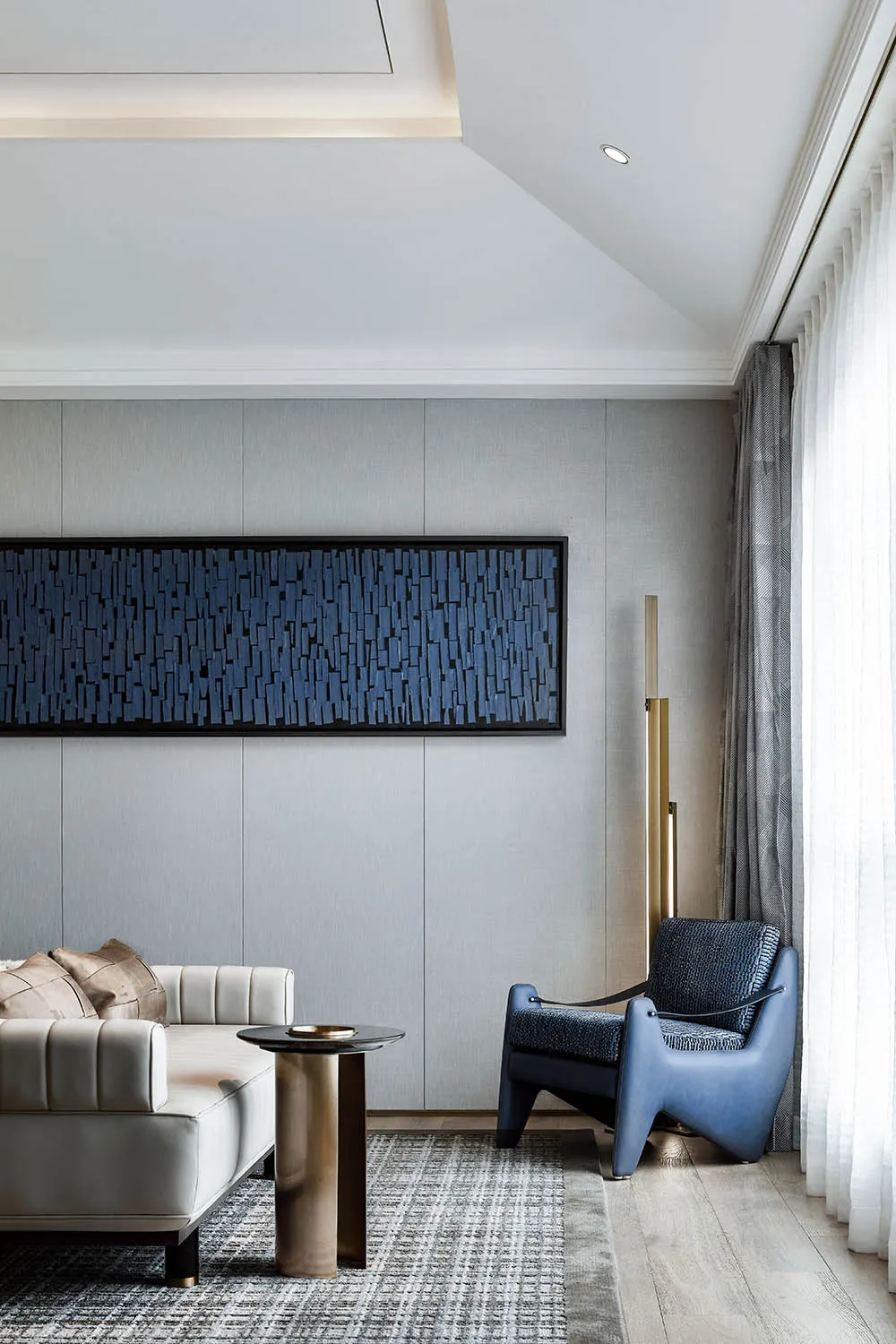 A modern living room featuring a fabric wall art piece and a combination of furniture with a blue accent chair and a white so