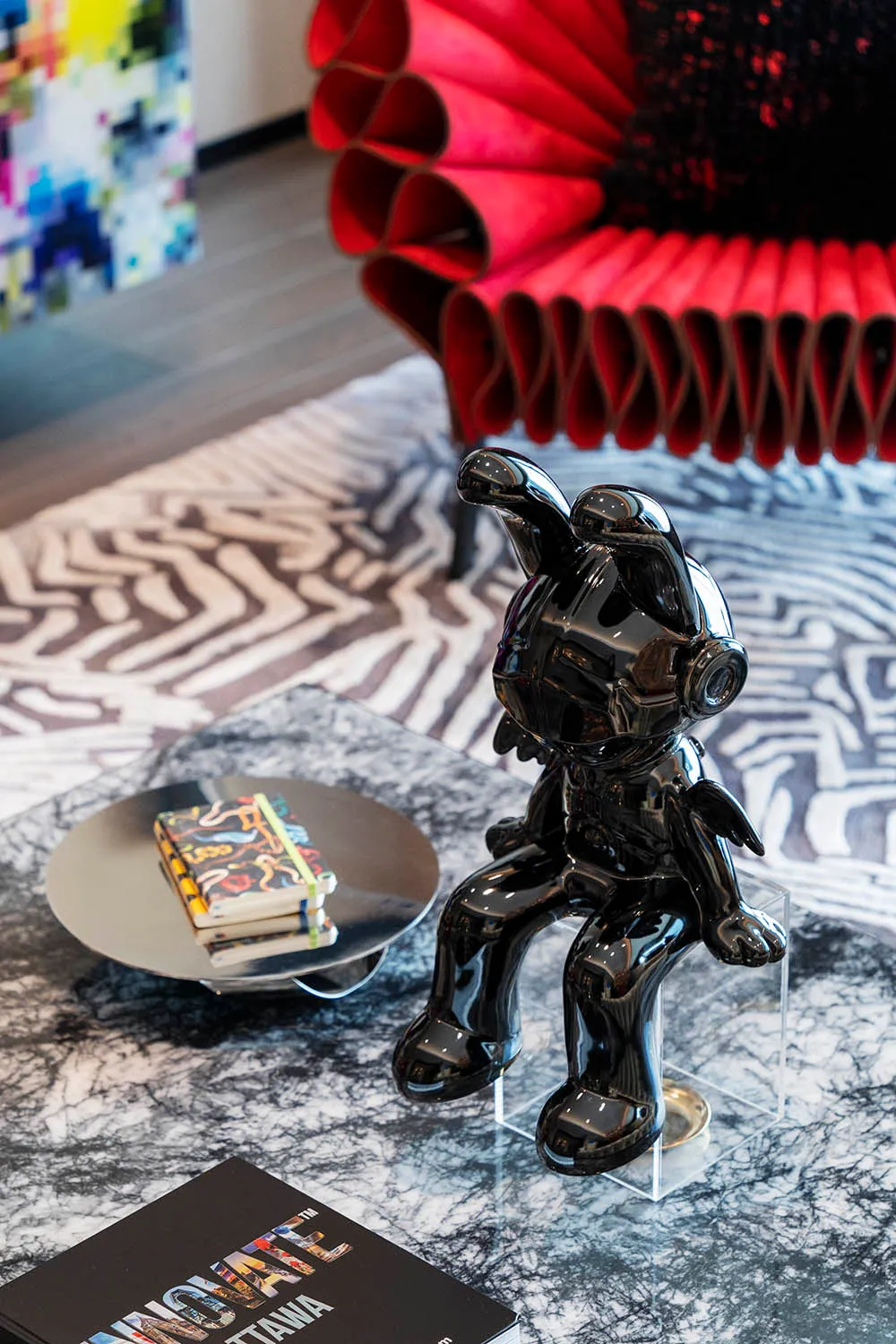 A shiny black metallic statue of a rabbit sitting on a glass table with a red textured chair in the background.