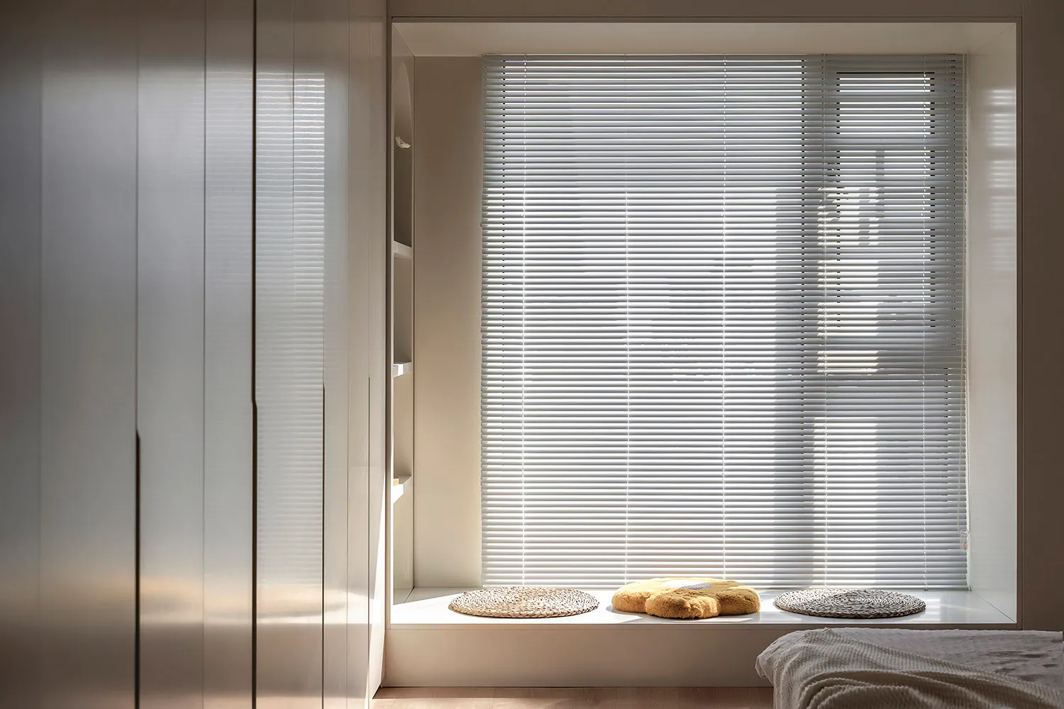 Minimalist bedroom with wooden blinds and plush cushions.