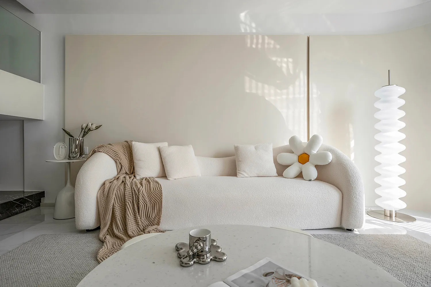 A minimalist living room with a white fabric sofa, cushions, and a round table.