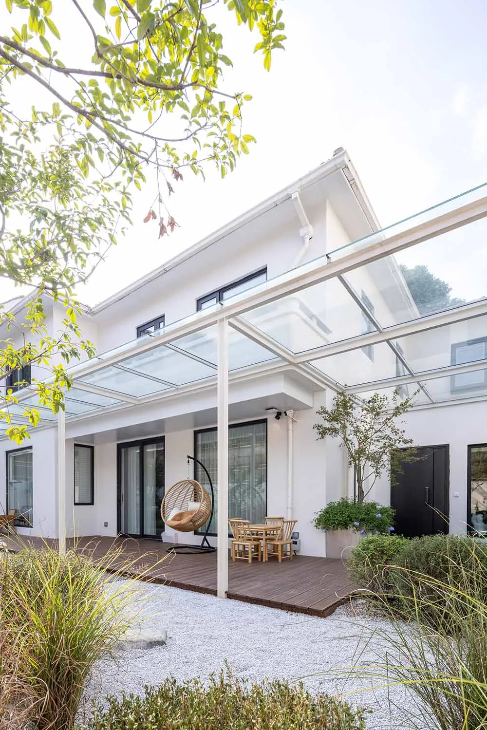 Modern patio with a glass roof and wooden deck, featuring minimalist design elements.