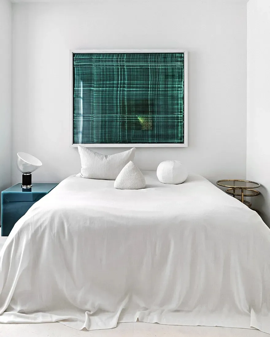 A modern bedroom with a green frame textile hanging above a neatly made bed.