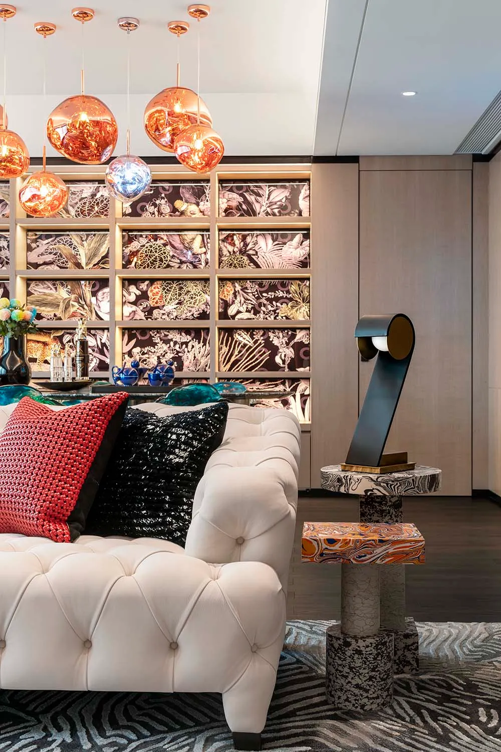 A modern living room featuring a velvet couch, patterned rug, and colorful lighting fixtures.