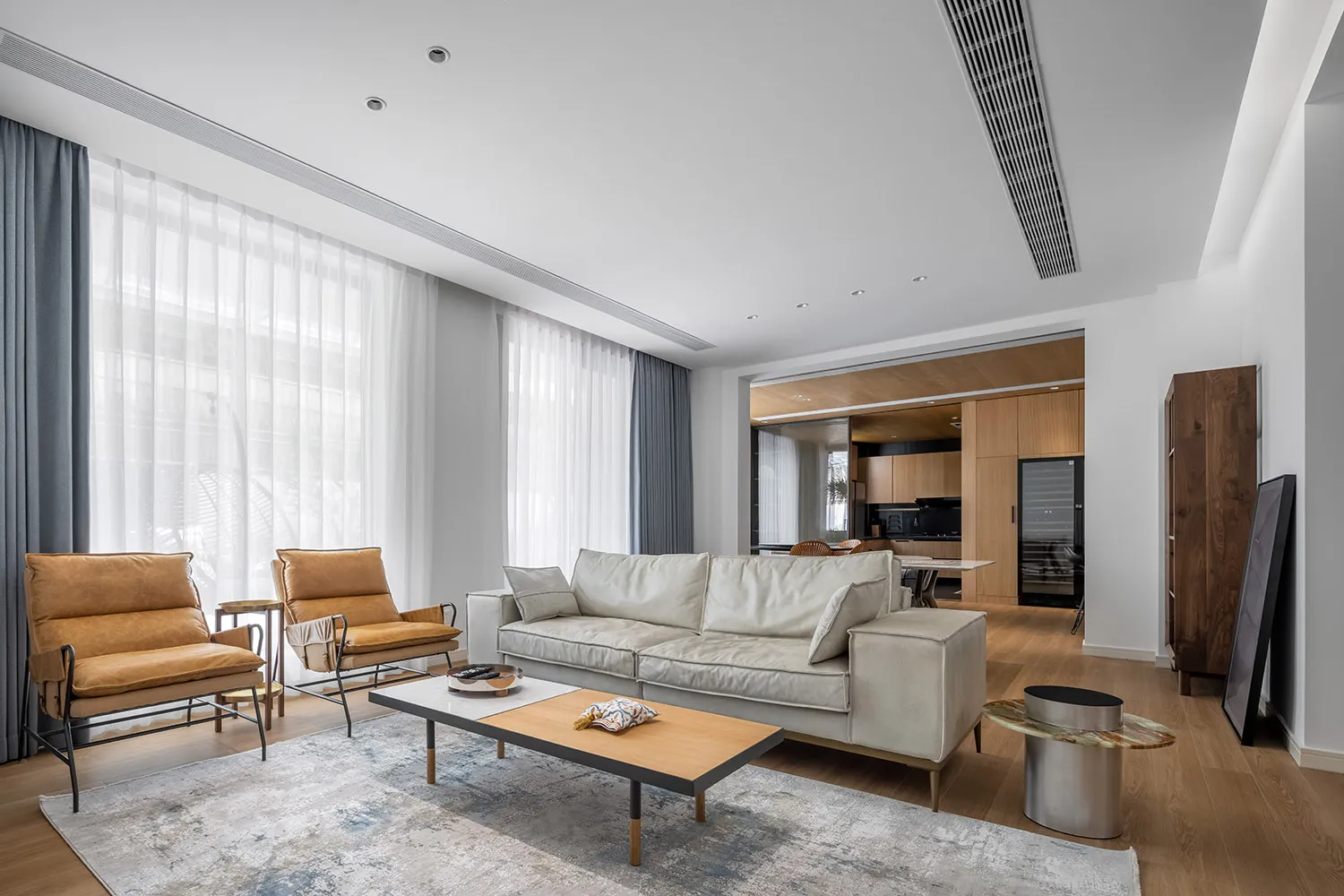 A modern living room with a neutral color palette featuring a white sofa, two brown armchairs, and a wooden coffee table.