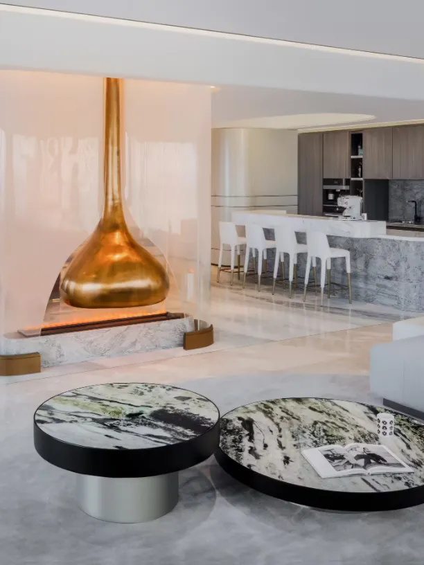 Modern lounge area with marble coffee tables, a glass pendant fireplace, and metal accents.
