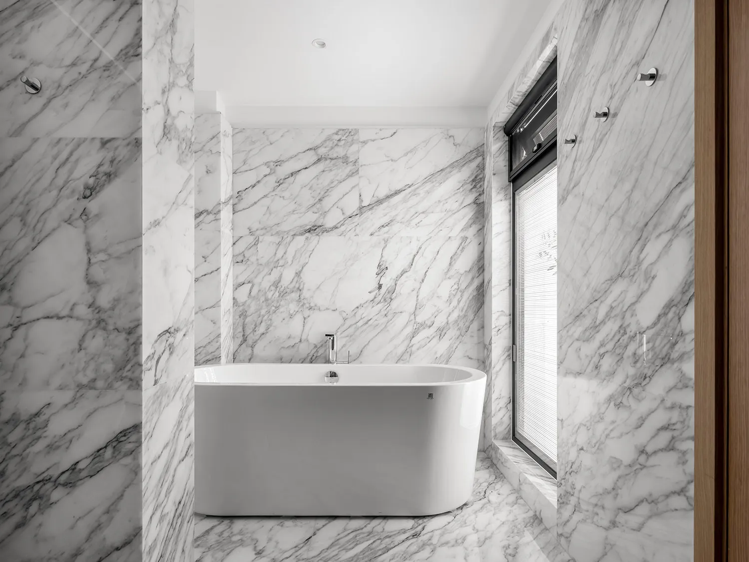 Modern bathroom with marble walls and floor, featuring a freestanding bathtub and a window.