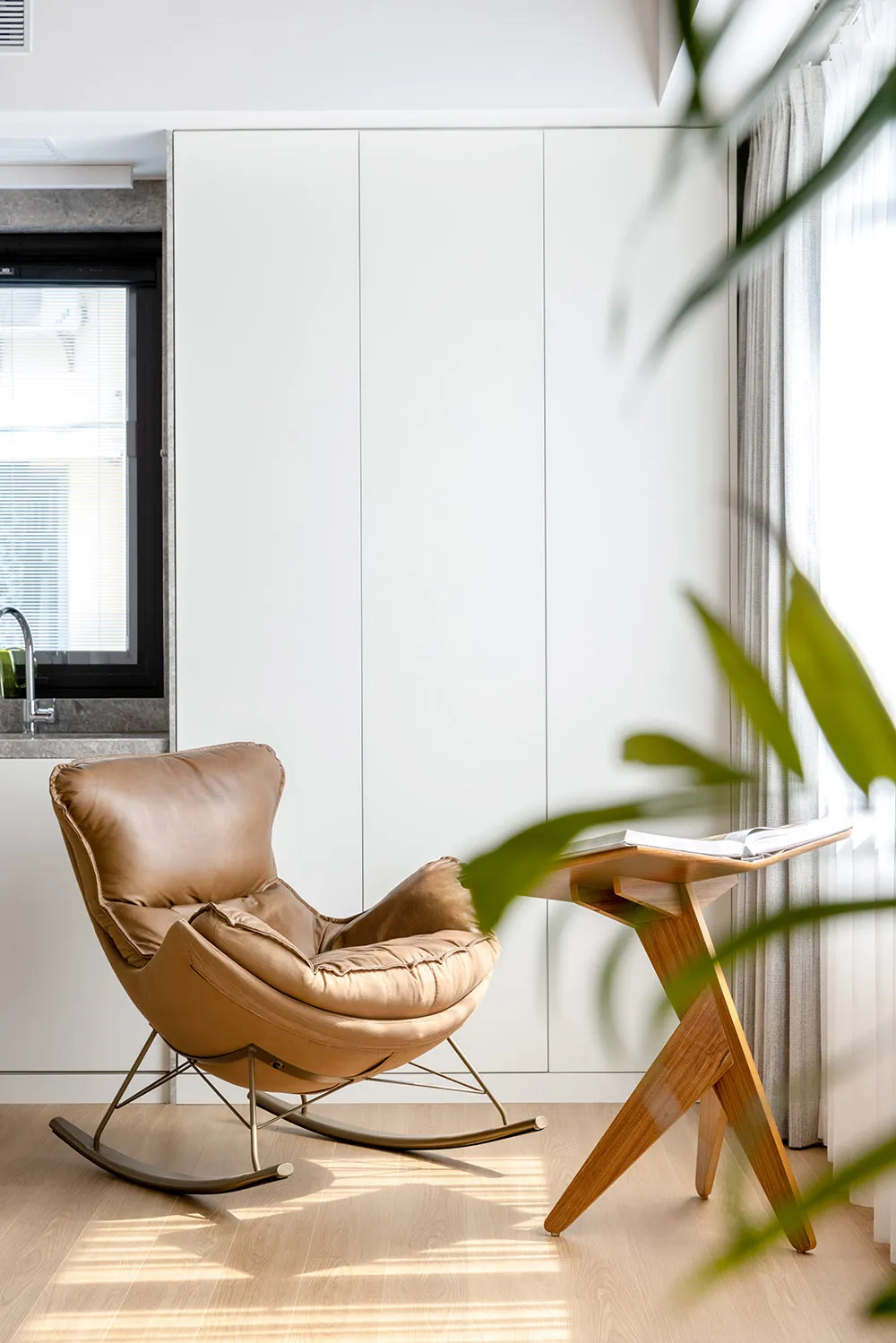 A minimalist home office with a comfortable wooden rocking chair and a sleek desk.