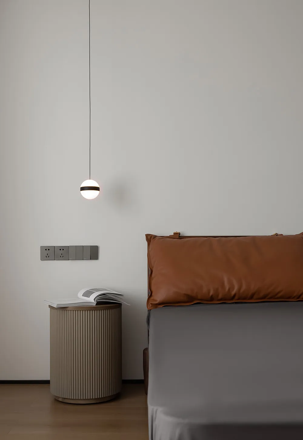 A modern bedroom featuring a brown leather cushion on a grey bed, photographed with a minimalist design style.