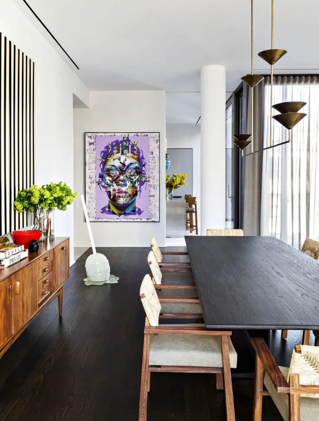 Modern dining room with a black wooden table, white cushioned chairs, and a colorful face painting.