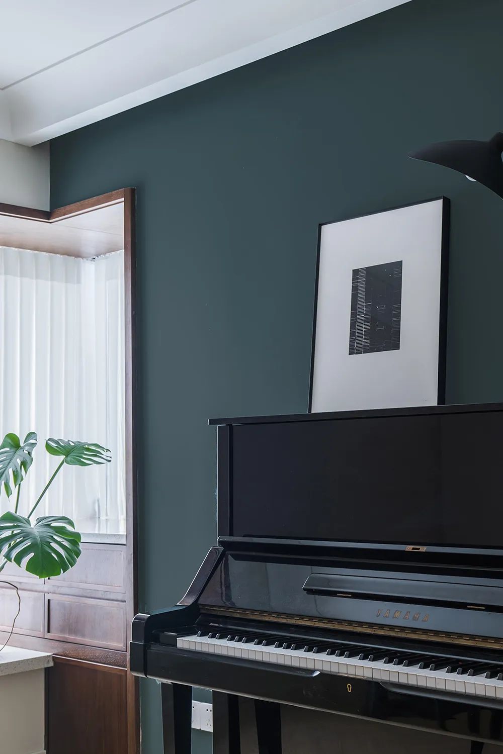 A modern interior design featuring a black piano in a well-lit room with green plant and framed artwork.