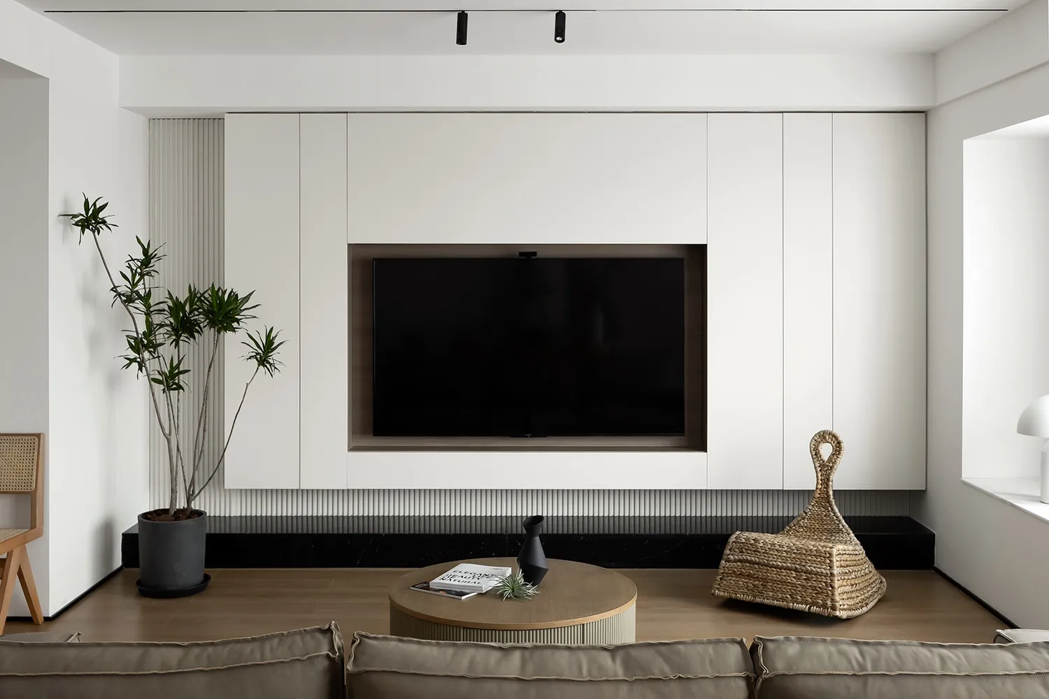 Modern, minimalist living room with white walls, a black marble shelf, a round wooden coffee table, and a flat-screen TV embe