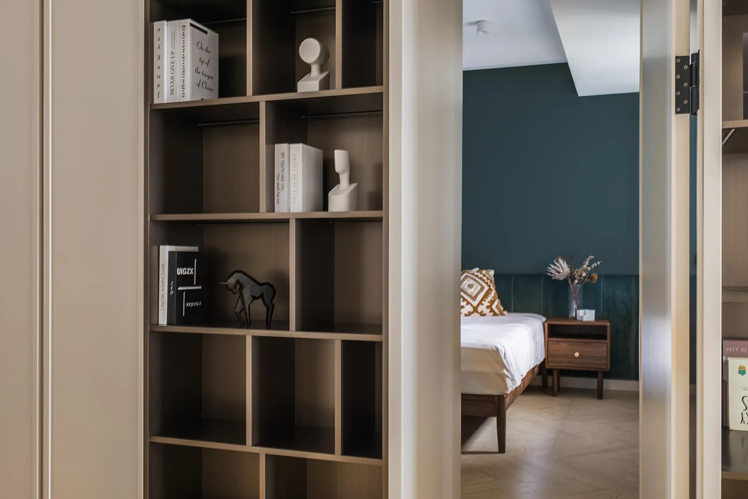 Modern bedroom with wooden shelving unit, white bedding, and dark green accent wall.