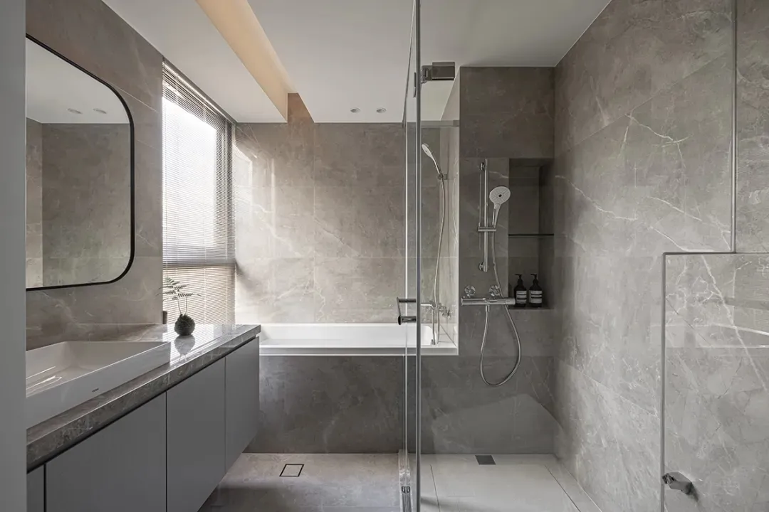 Modern bathroom with marble tiles, white bathtub, glass shower enclosure, and minimalist design.