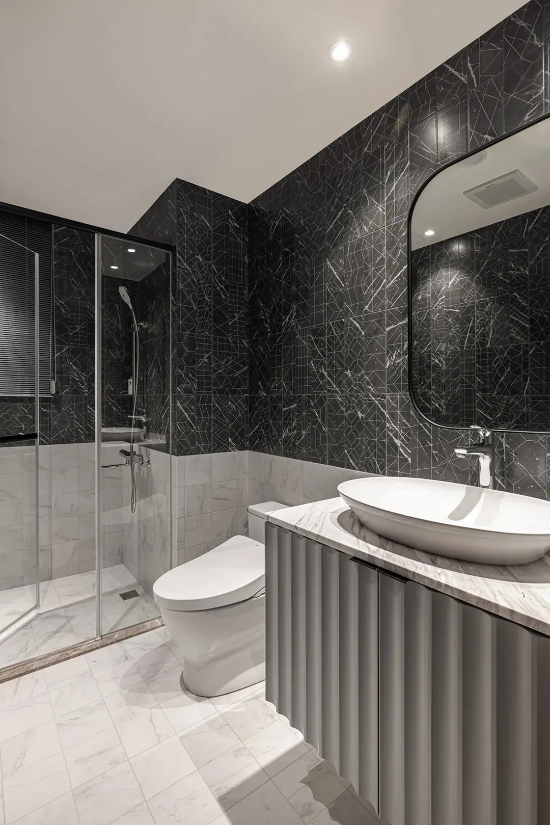 A modern residential bathroom with marble tiles, metal accents, and a white toilet.