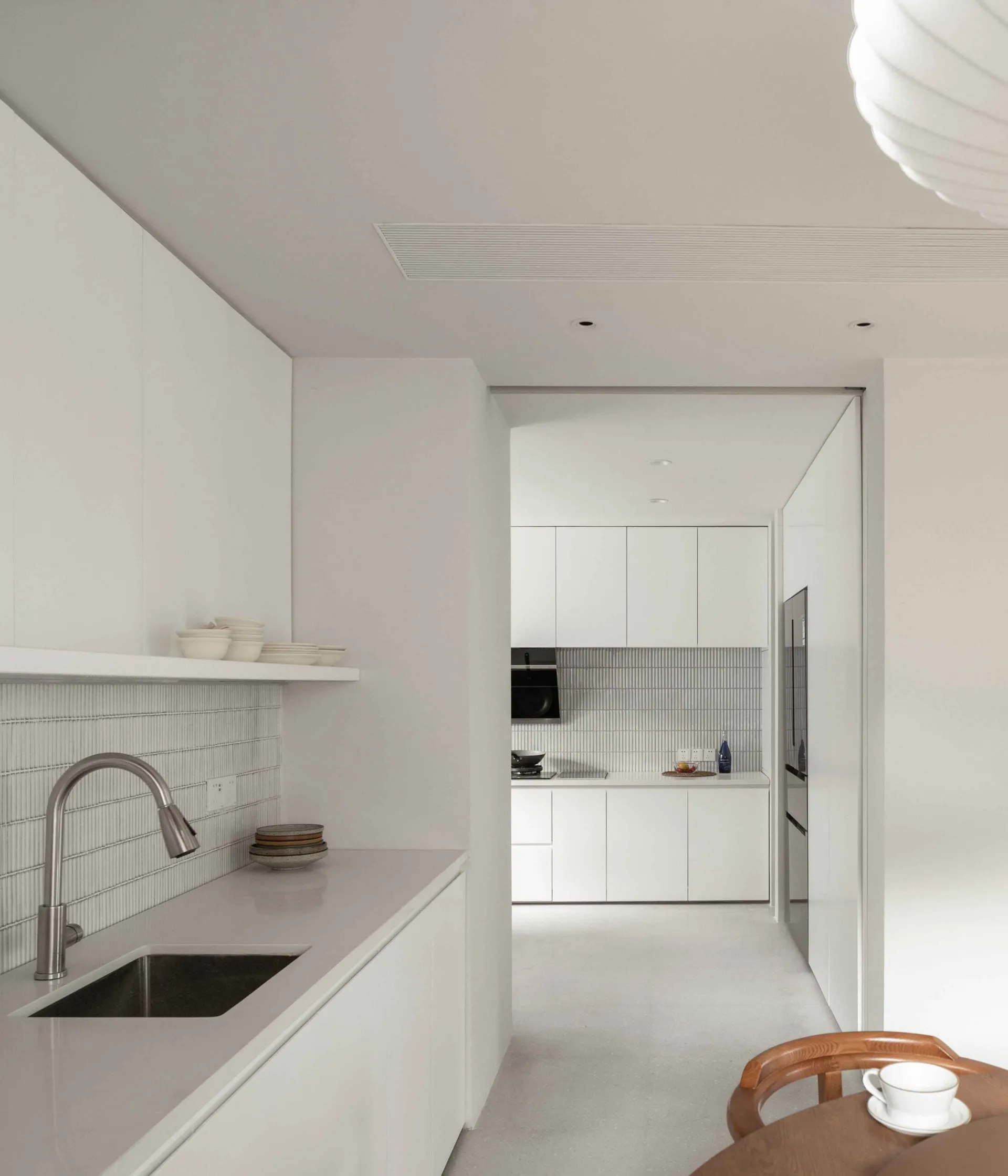 A minimalist kitchen with white cabinets, a stainless steel sink, and a light fixture hanging above the dining area.