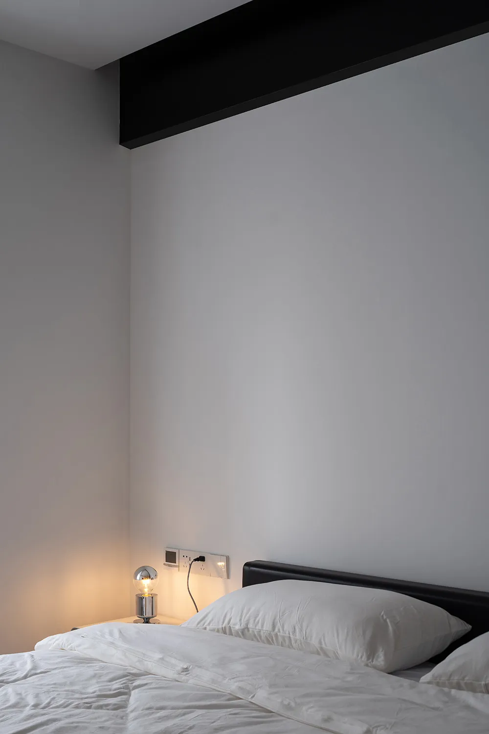 Minimalist bedroom with white pillows on an unmade bed, featuring a single light bulb on a bedside table.