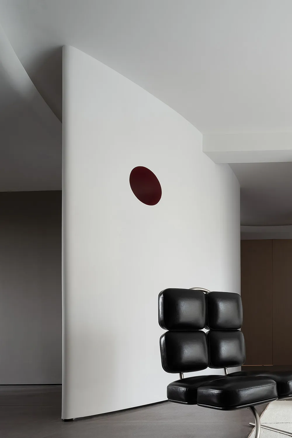 A minimalist interior space featuring a black leather cushion and a red circular feature on the wall.