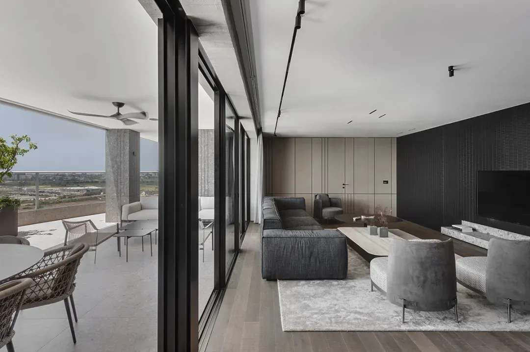 Living room with grey sofa, armchairs, and coffee table, large floor-to-ceiling windows, and balcony with outdoor seating and