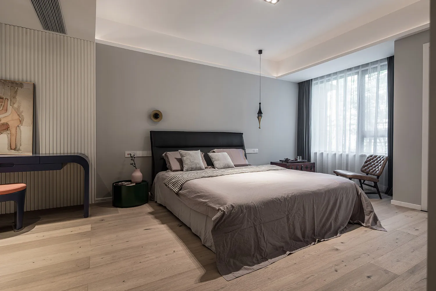 A minimalist bedroom with light wood flooring, a gray bed, and a black headboard.