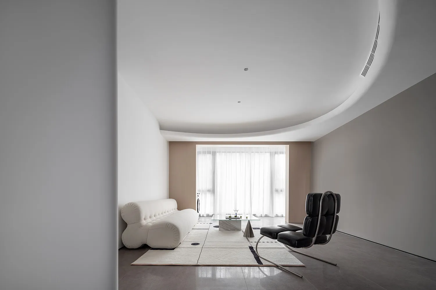 A minimalist living room with a fabric sofa, leather chairs, and a glass coffee table.
