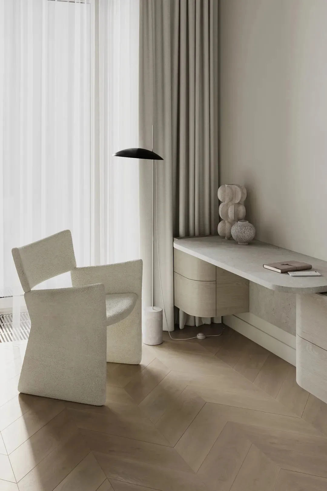 A minimalist residential interior featuring marble and concrete materials, with a modern chair, a desk with a lamp, and a war