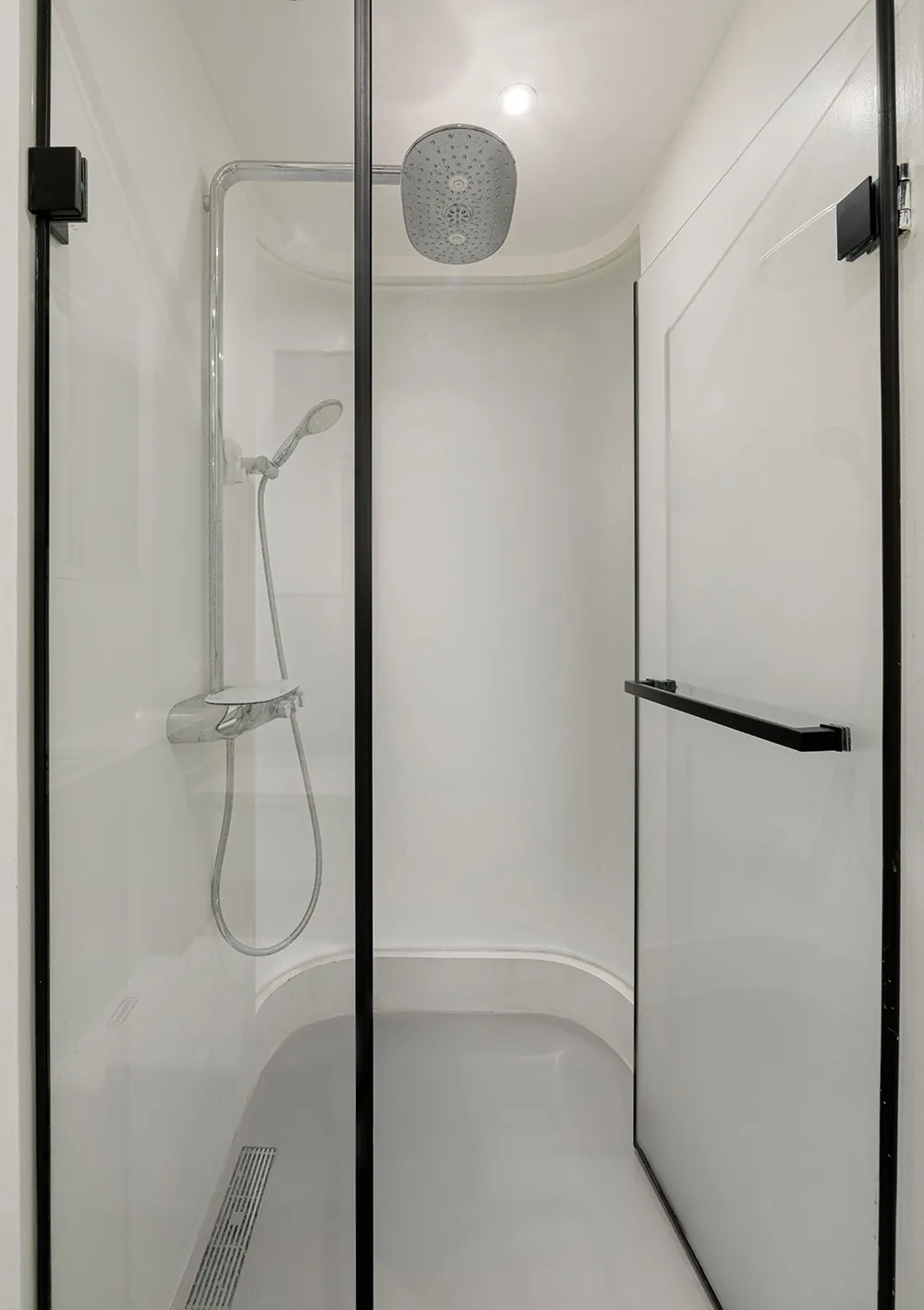 A sleek, minimalist bathroom with a glass shower enclosure and white fixtures.