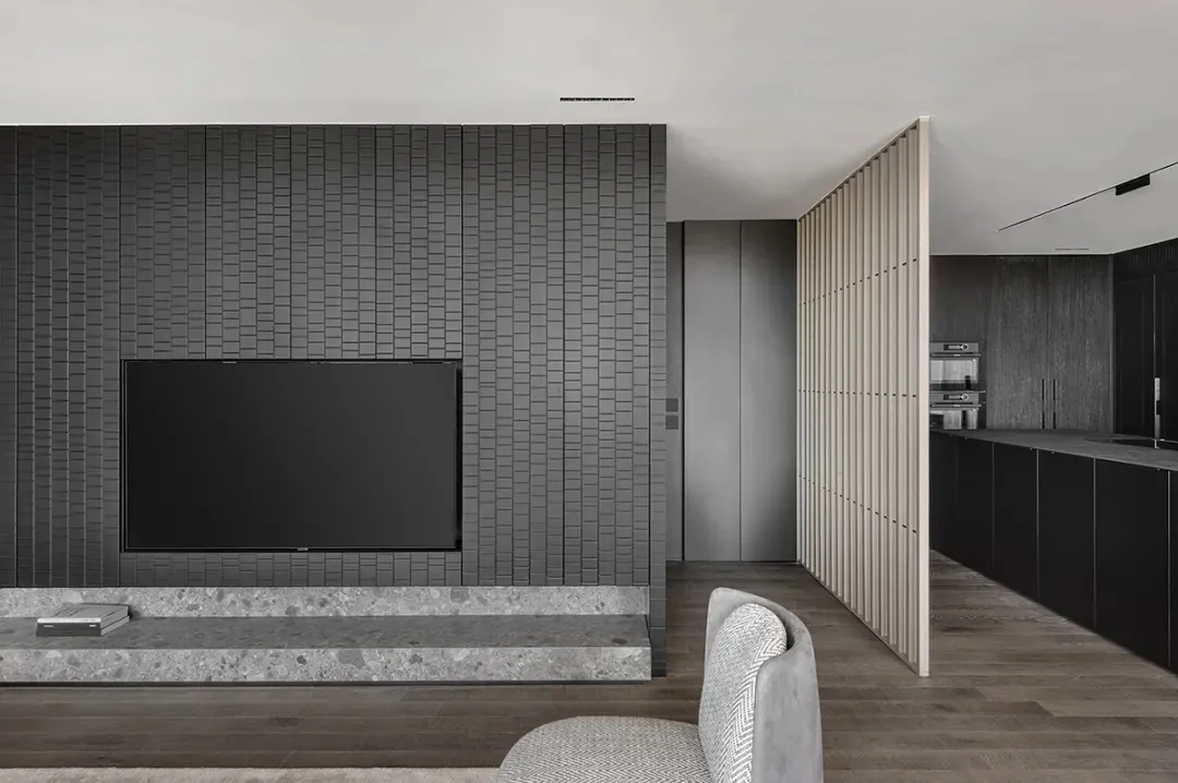 A modern living room with grey tiles, a flat-screen TV on a marble stand, and a chair with a white and grey patterned upholst