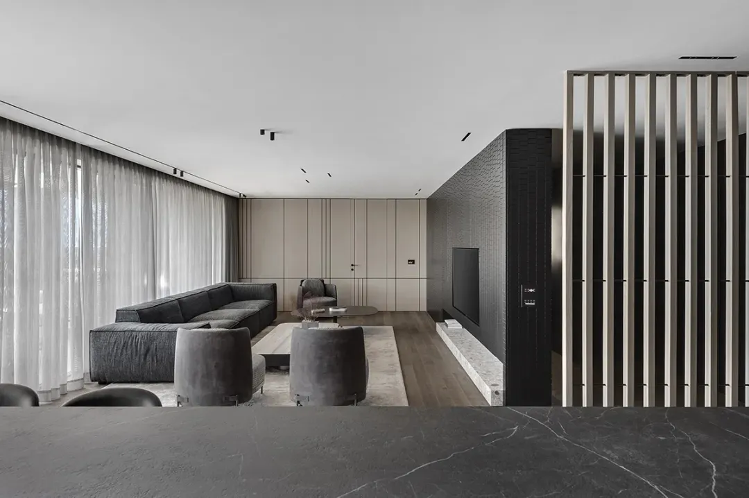 A modern, minimalist living room with dark wood flooring, light-colored walls, and mixed materials including leather furnitur