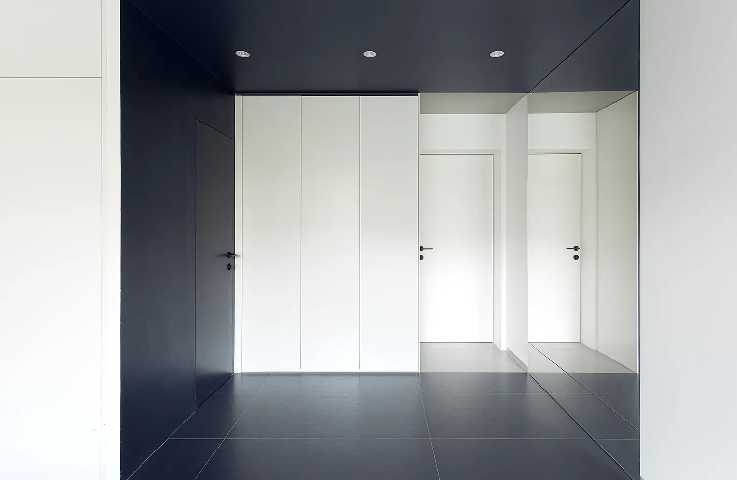 A minimalist white hallway with black accent walls and black-tiled floor.