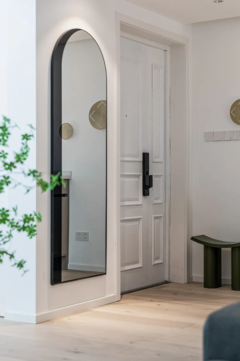 A white entrance hall featuring a large, framed mirror with an arched top on the left side, a white paneled door on the right