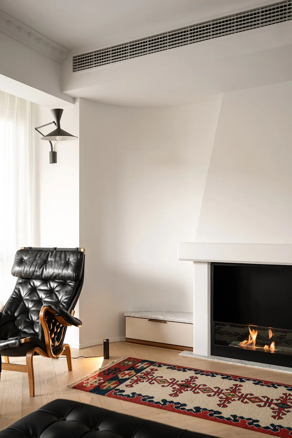 A modern living room with a white fireplace, leather chair, and patterned carpet.