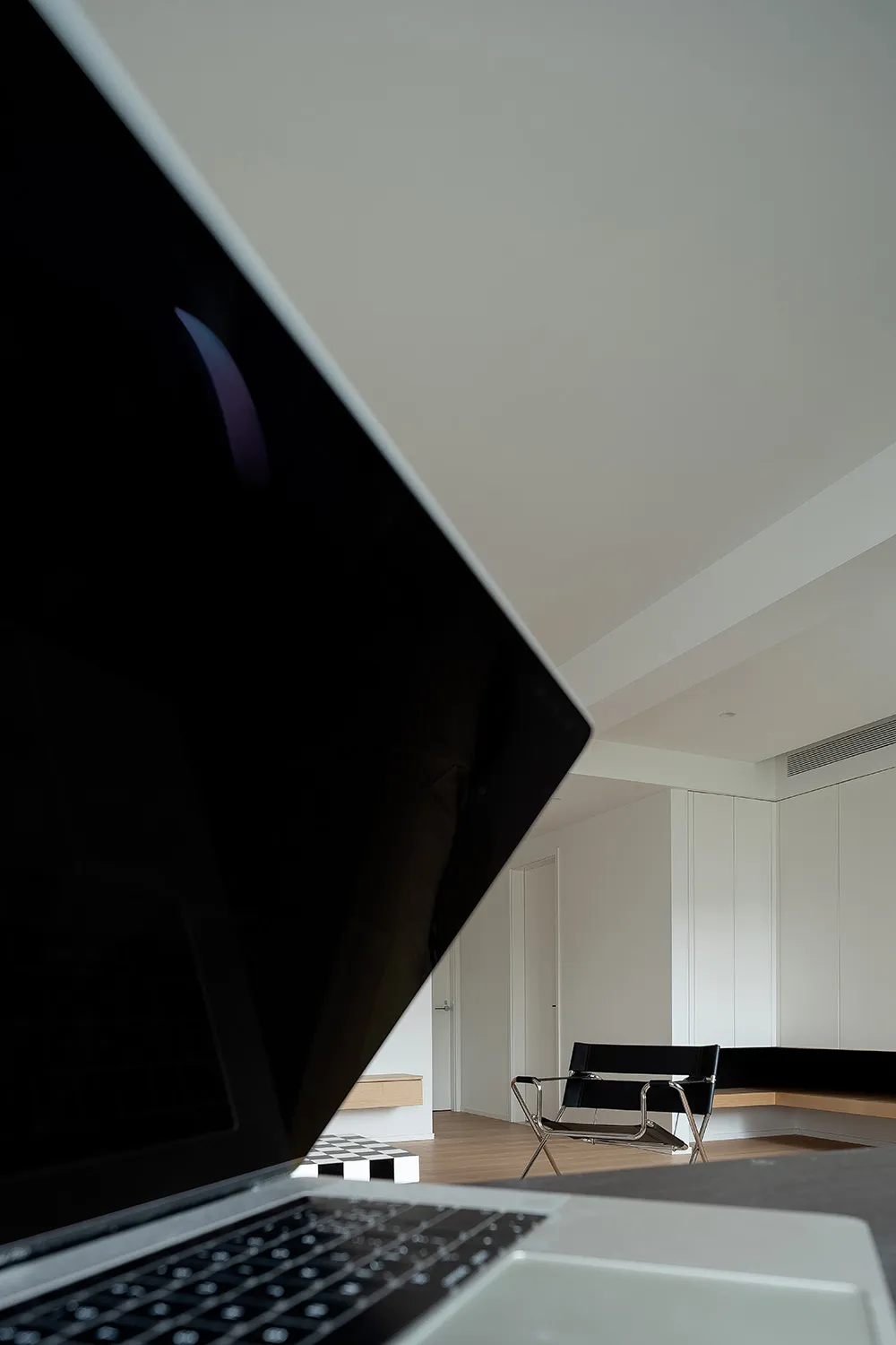 A minimalist home office setup featuring a sleek, modern desk and chair in a well-lit, white room with wooden flooring.