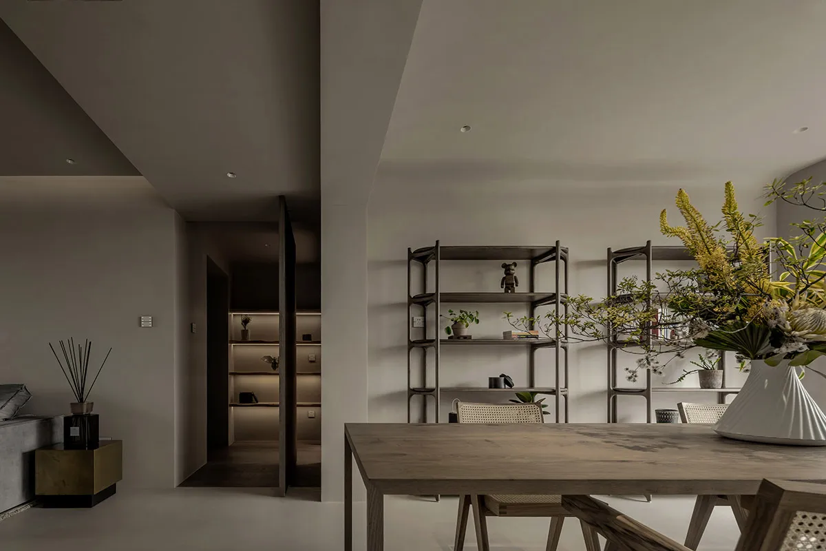 A minimalist dining room featuring wooden furniture and shelves with decorative items.