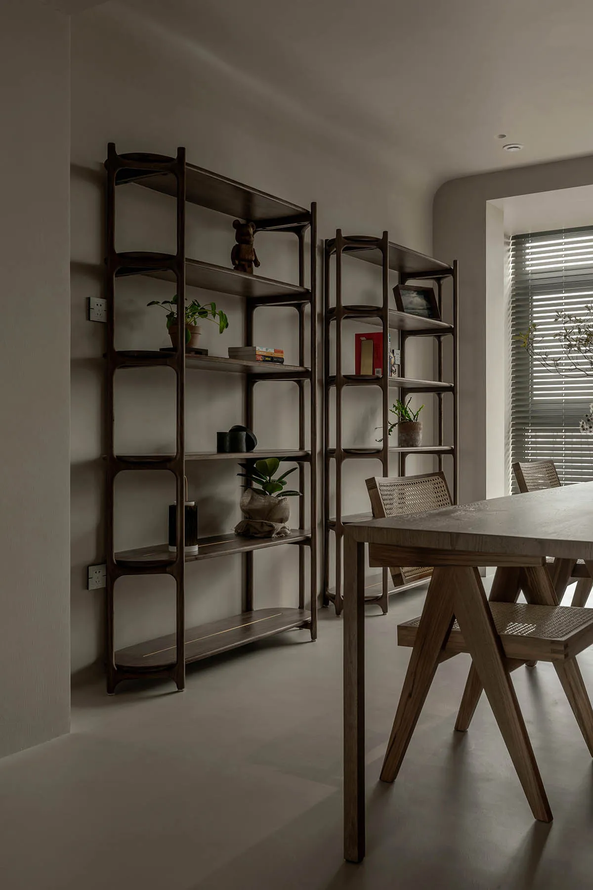 A minimalist dining room featuring wood shelves with various decorative items and a wooden dining table.
