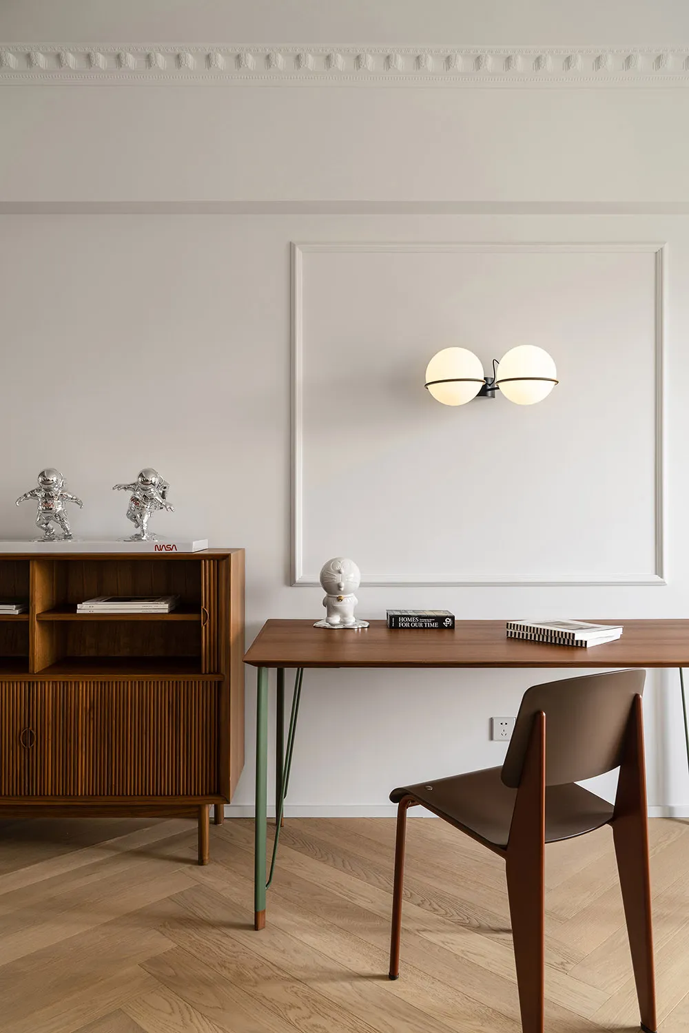 Minimalist home office featuring a wooden desk and chair against a white wall, with decorative items and lighting.