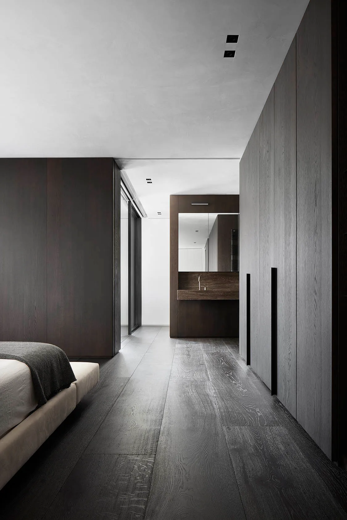 Modern bedroom suite with gray wood flooring and a concrete countertop, featuring a white bed.