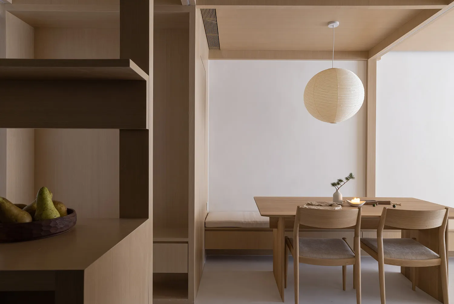 A minimalist dining room featuring wooden furniture and a round paper lantern pendant light.