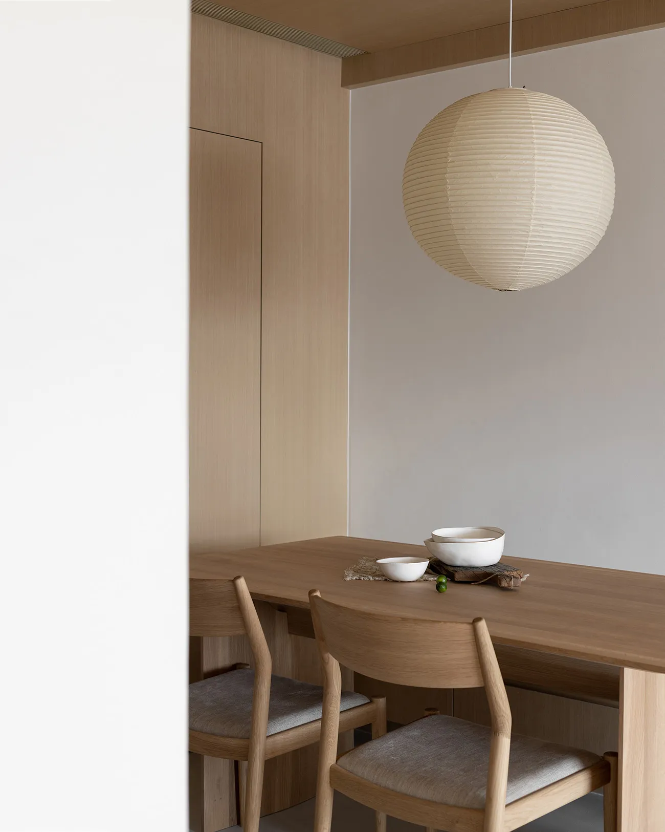A minimalist dining room with a wooden table and chairs, featuring a spherical pendant light and simple decor.