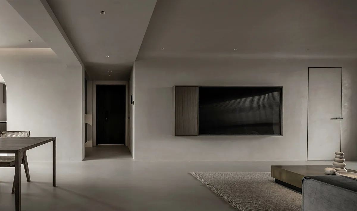 A modern minimalist living room with a concrete floor, dark wood furniture, and a large TV mounted on the wall.