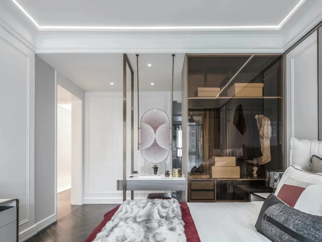 A modern bedroom featuring a bed with a fur blanket, white and burgundy pillows, and a metal-framed glass closet.
