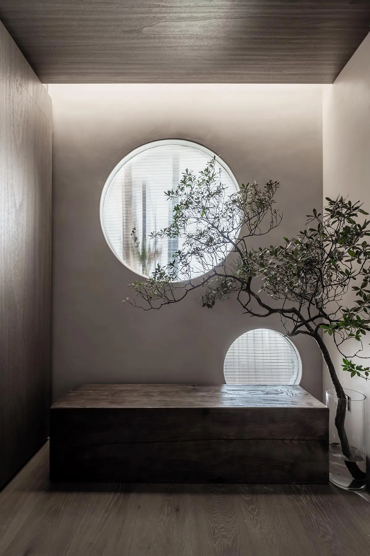 A modern living space featuring a wooden sofa with water droplets on it, set against a wall with two circular windows and a w